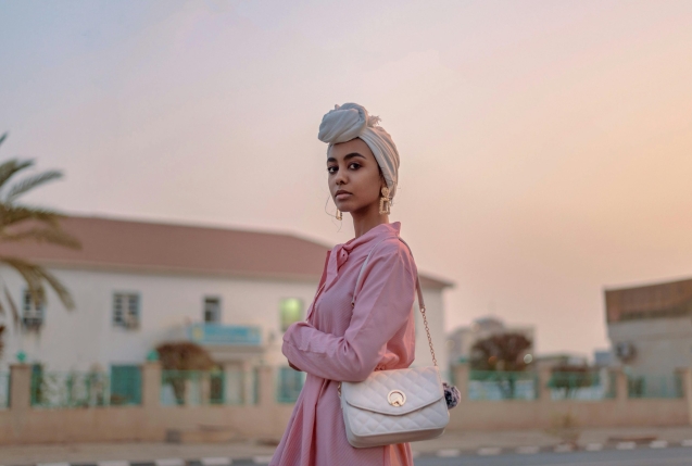 Stylish woman in pink dress with turban, posing outdoors at sunset.