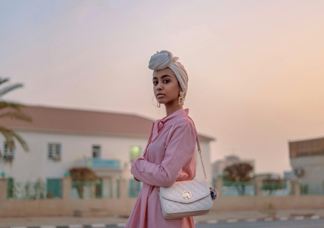 Stylish woman in pink dress with turban, posing outdoors at sunset.