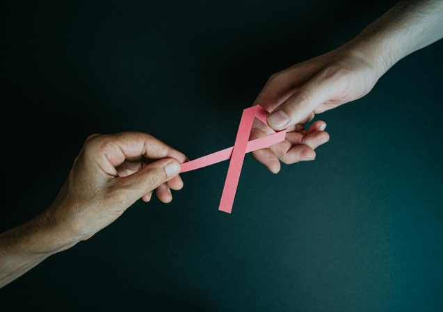 Two hands exchanging a pink ribbon symbolizing breast cancer awareness and support.
