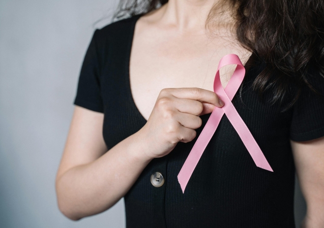 Close-up of a woman holding a pink ribbon symbolizing breast cancer awareness and support.