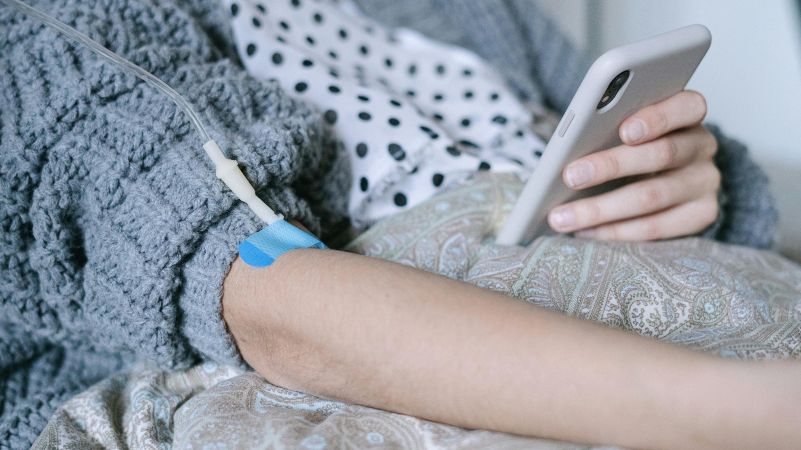 A woman receiving intravenous therapy for cancer treatment while using her phone, symbolizing connection and hope.