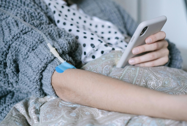 A woman receiving intravenous therapy for cancer treatment while using her phone, symbolizing connection and hope.