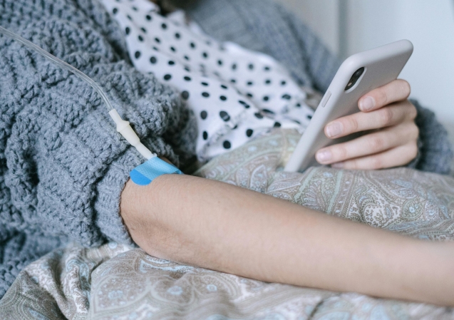 A woman receiving intravenous therapy for cancer treatment while using her phone, symbolizing connection and hope.